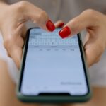 Hands of a Woman With Red Nails Typing on a Smartphone