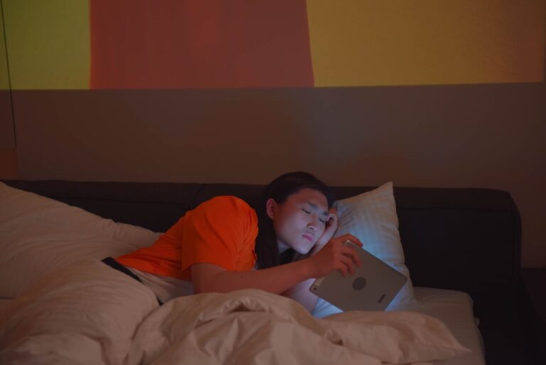 Man in Orange Shirt Holding Silver Digital Tablet