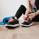 slender female athlete tying shoelaces near sport accessories