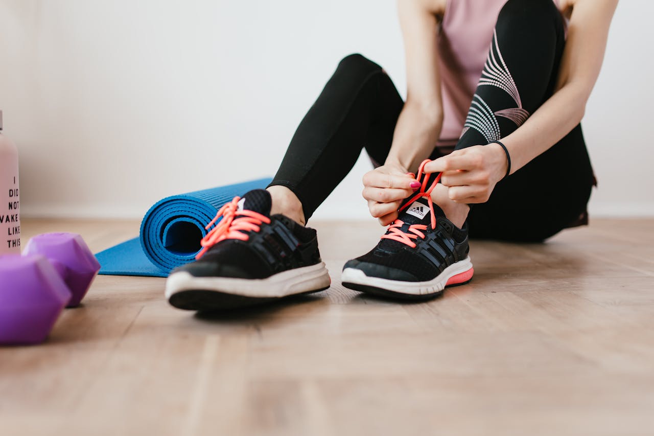 slender female athlete tying shoelaces near sport accessories