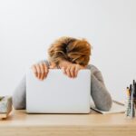 A Woman Leaning and Holding onto a Laptop on a Wooden Table