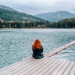 Person sitting on a wooden dock near a calm lake, enjoying a peaceful weekend getaway.