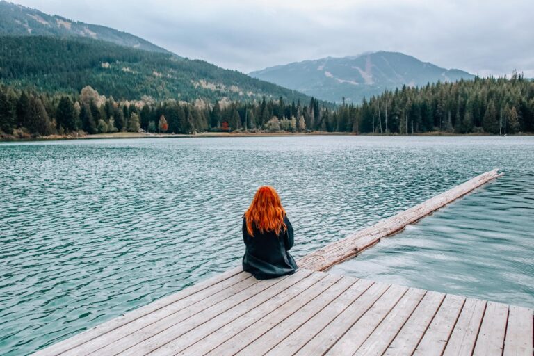 Person sitting on a wooden dock near a calm lake, enjoying a peaceful weekend getaway.