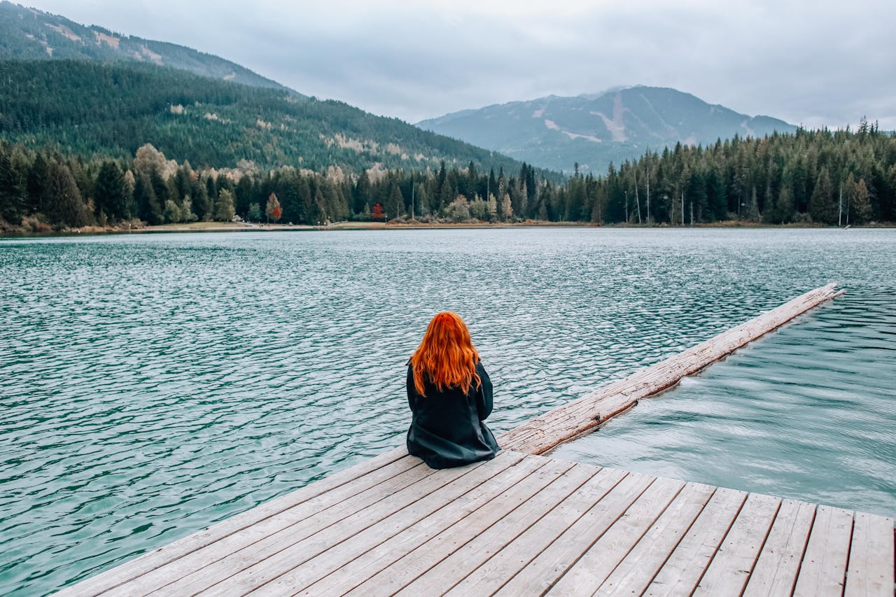 Person sitting on a wooden dock near a calm lake, enjoying a peaceful weekend getaway.