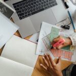 A person writing on a paper and using laptop