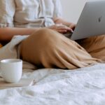 Woman Lounging With Laptop And Cup Of Coffee On The Bed
