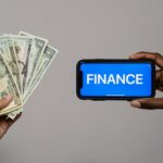 Finance word written in the phone with blue background, with some currency notes in other hand