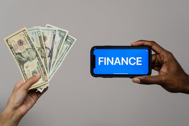 Finance word written in the phone with blue background, with some currency notes in other hand