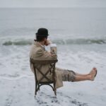 Man in Brown Jacket Sitting on Brown Chair on Beach