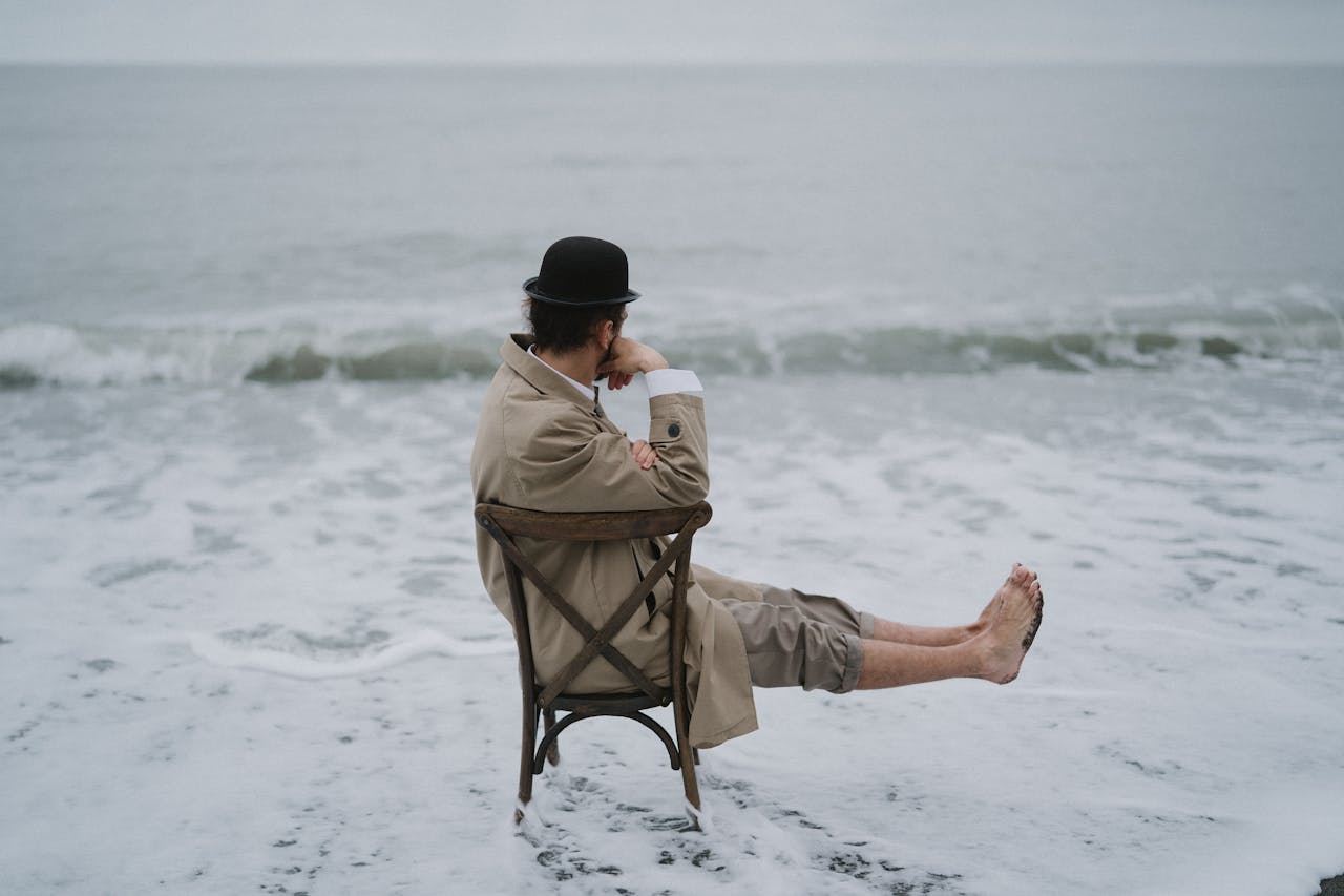 Man in Brown Jacket Sitting on Brown Chair on Beach