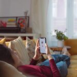 A Person Lying on Sofa Holding a Smartphone with a Person's Profile on Screen