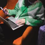A Woman using a Smartphone and a Laptop while Sitting on an Armchair
