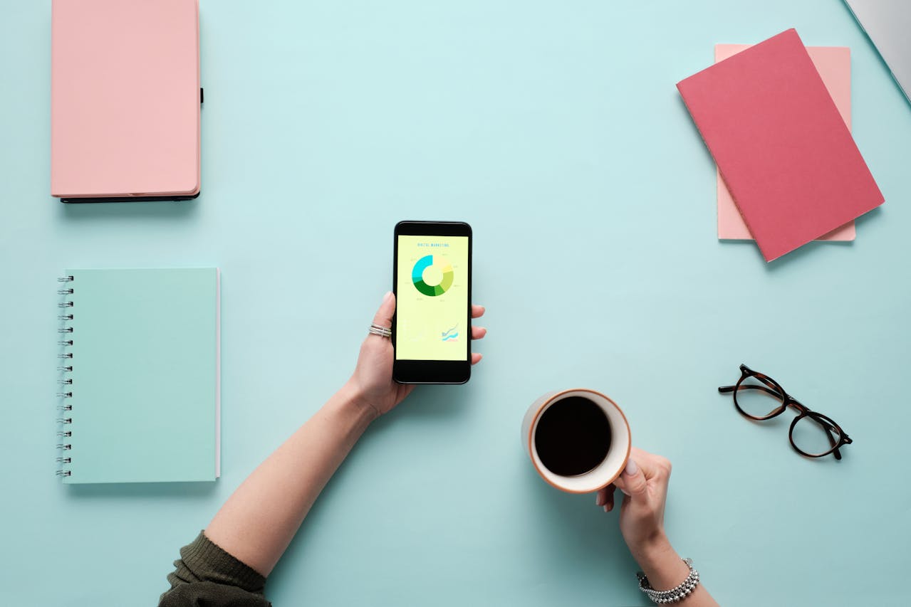 Person holding a phone beside a cup of coffee in a clean, minimalist workspace.