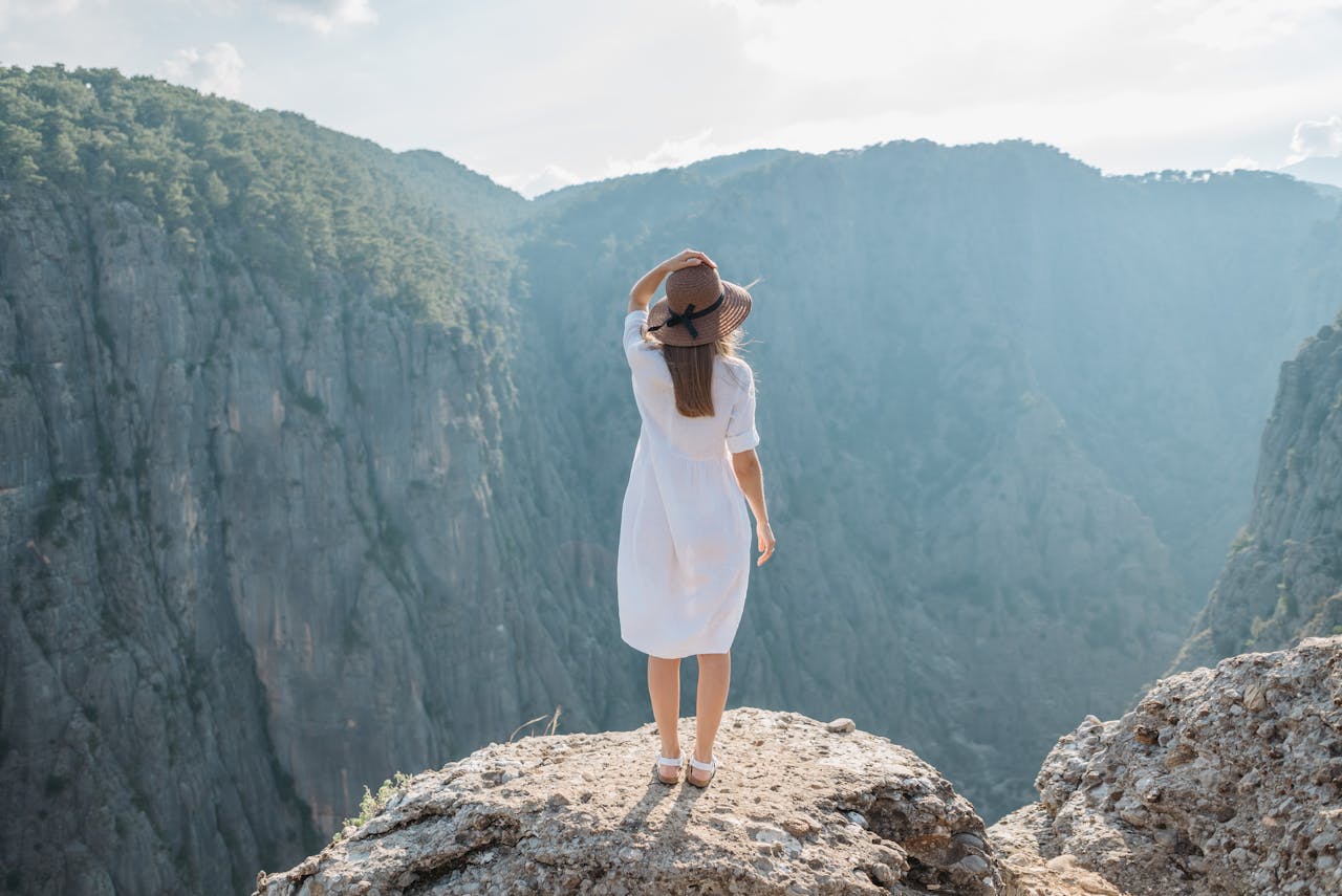 Woman standing on a mountain cliff during sunrise, symbolizing the freedom and confidence of solo travel.